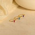 Three Pave Marquise Birthstone Rings with red, blue, and purple personalized stones are displayed on a beige surface with a fabric background—perfect as custom birthstone rings for any special occasion.