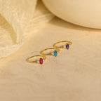 Three Pave Marquise Birthstone Rings with red, blue, and purple personalized stones are displayed on a beige surface with a fabric background—perfect as custom birthstone rings for any special occasion.