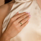 A woman's manicured hand rests on her chest, adorned with the Pave Triple Birthstone Ring—personalized jewelry with green gemstones set in gold.
