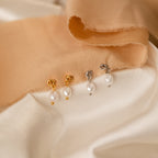 Two pairs of Dainty Knot Pearl Earrings—one gold, one silver—are displayed on cream and peach fabric, exuding classic charm and timeless elegance.