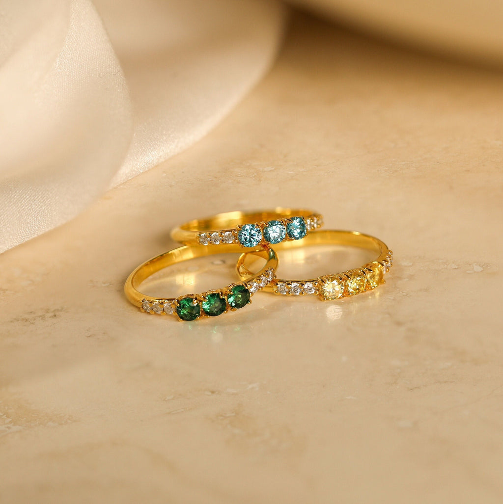 The Pave Triple Birthstone Ring features three gold bands with customizable green, blue, and yellow stones plus clear accents—an elegant personalized jewelry piece, perfect as a custom birthstone gift for any special occasion.