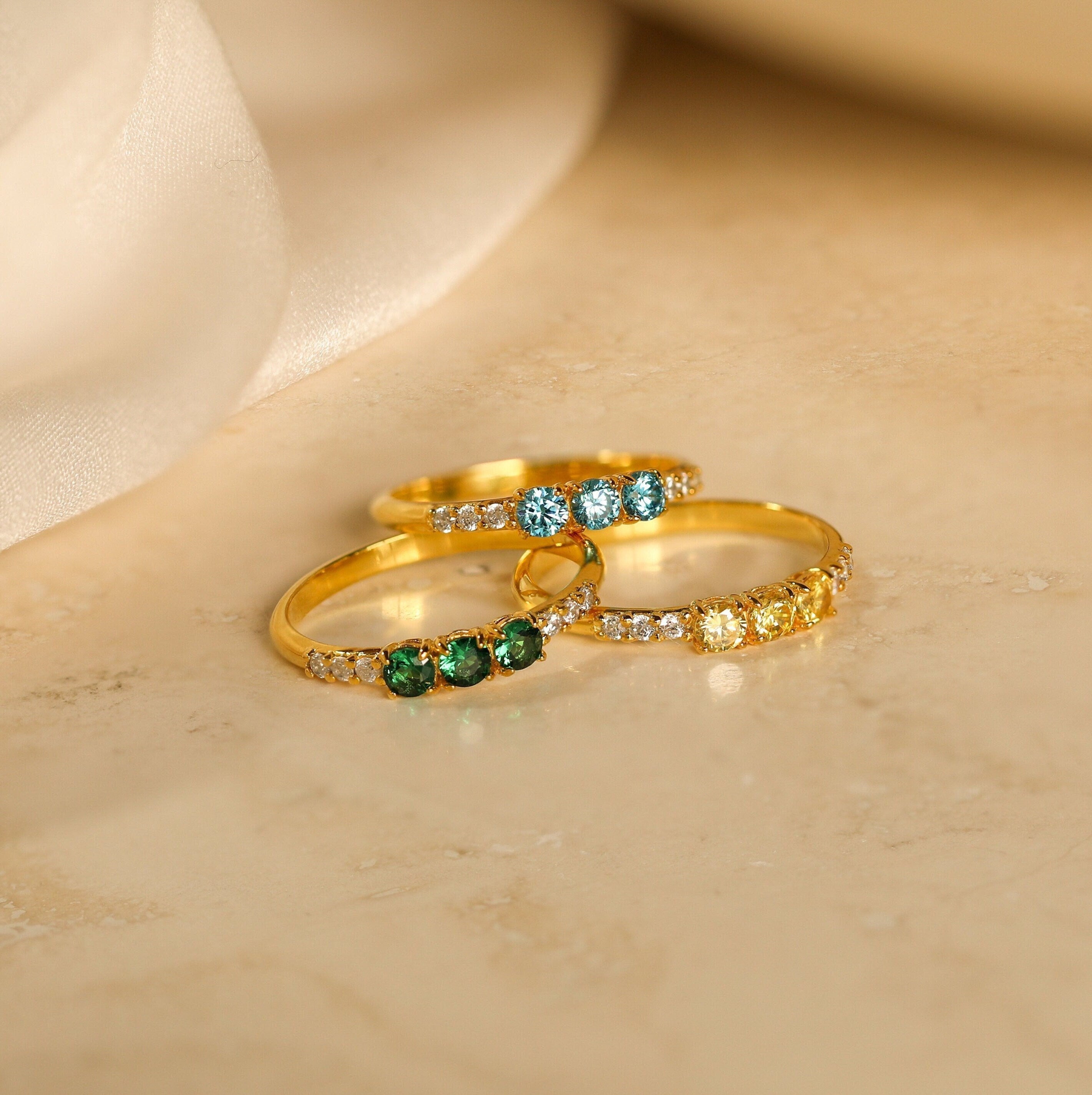 The Pave Triple Birthstone Ring features three gold bands with customizable green, blue, and yellow stones plus clear accents—an elegant personalized jewelry piece, perfect as a custom birthstone gift for any special occasion.