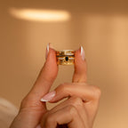 A hand with manicured nails displays a stack of rings, featuring the Pave Oval Birthstone Ring, against a beige background.