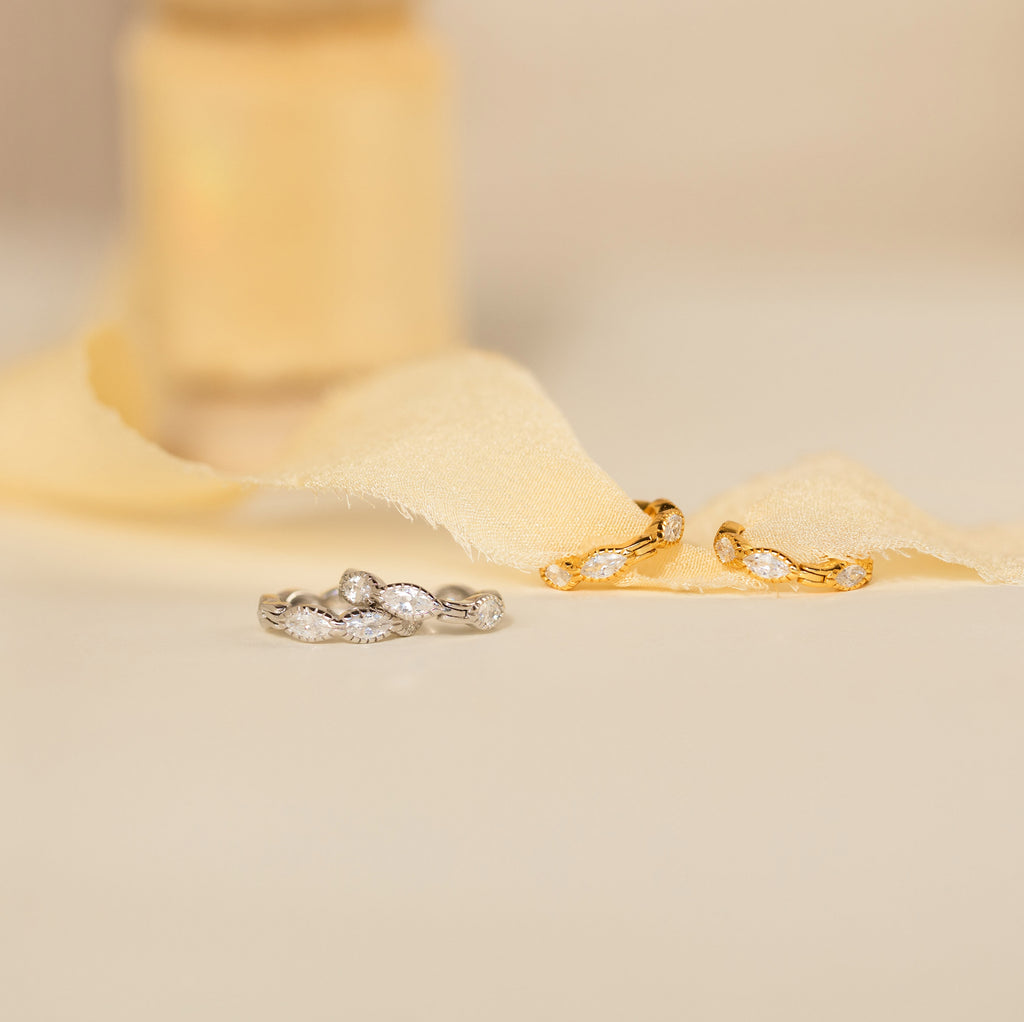 Two pairs of Marquise Inlay Huggies—one silver, one gold—are displayed on soft cream fabric.