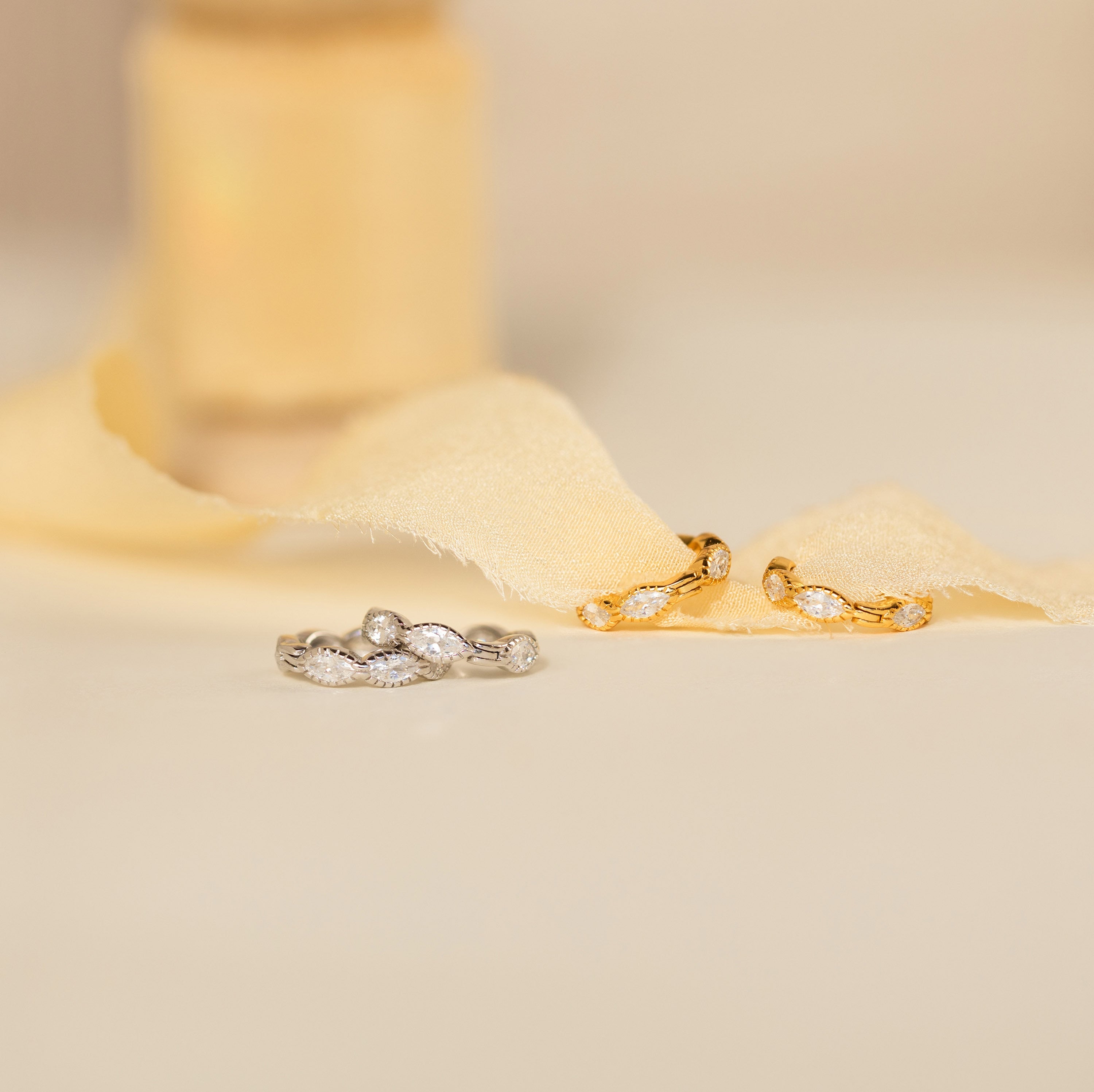 Two pairs of Marquise Inlay Huggies—one silver, one gold—are displayed on soft cream fabric.