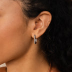 Close-up of a woman's ear wearing trendy Twisted Link Hoops with a ribbed texture, set against her curly dark hair.