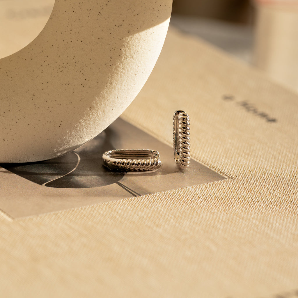 Twisted Link Hoops displayed on beige fabric under soft natural light.