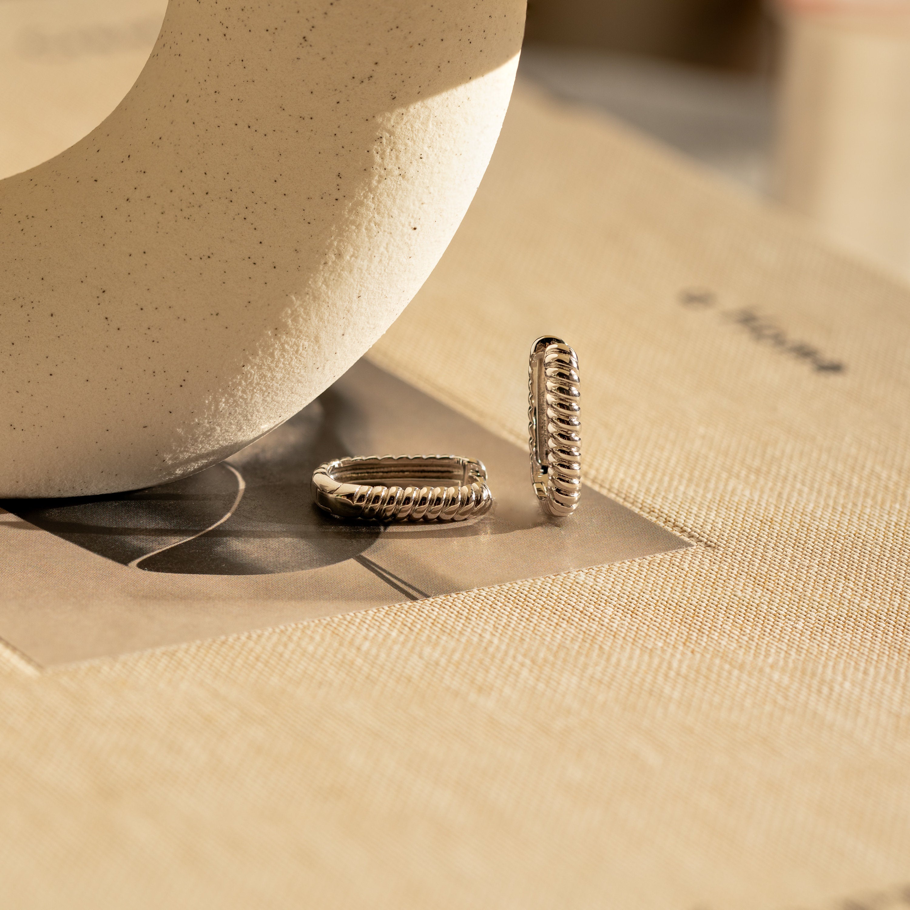 Twisted Link Hoops displayed on beige fabric under soft natural light.