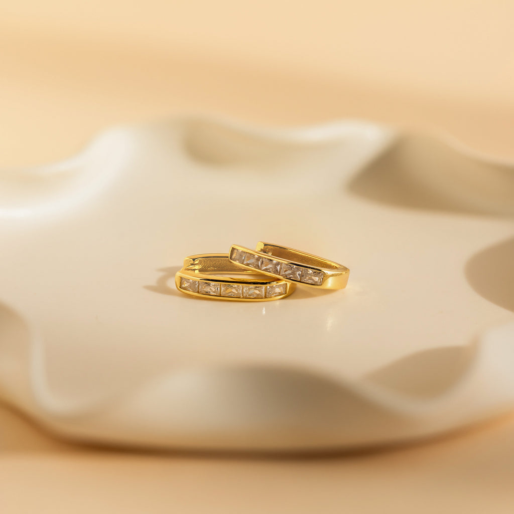 A pair of Baguette Link Hoops rests elegantly on a white plate, highlighting the timeless charm of minimalist geometric gold earrings.