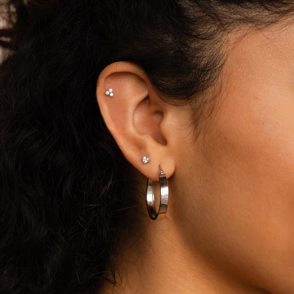 Close-up of a woman's ear wearing three small stud earrings and one standout Thick Hoops earring.