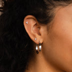 Close-up of a woman's ear wearing three small stud earrings and one standout Thick Hoops earring.