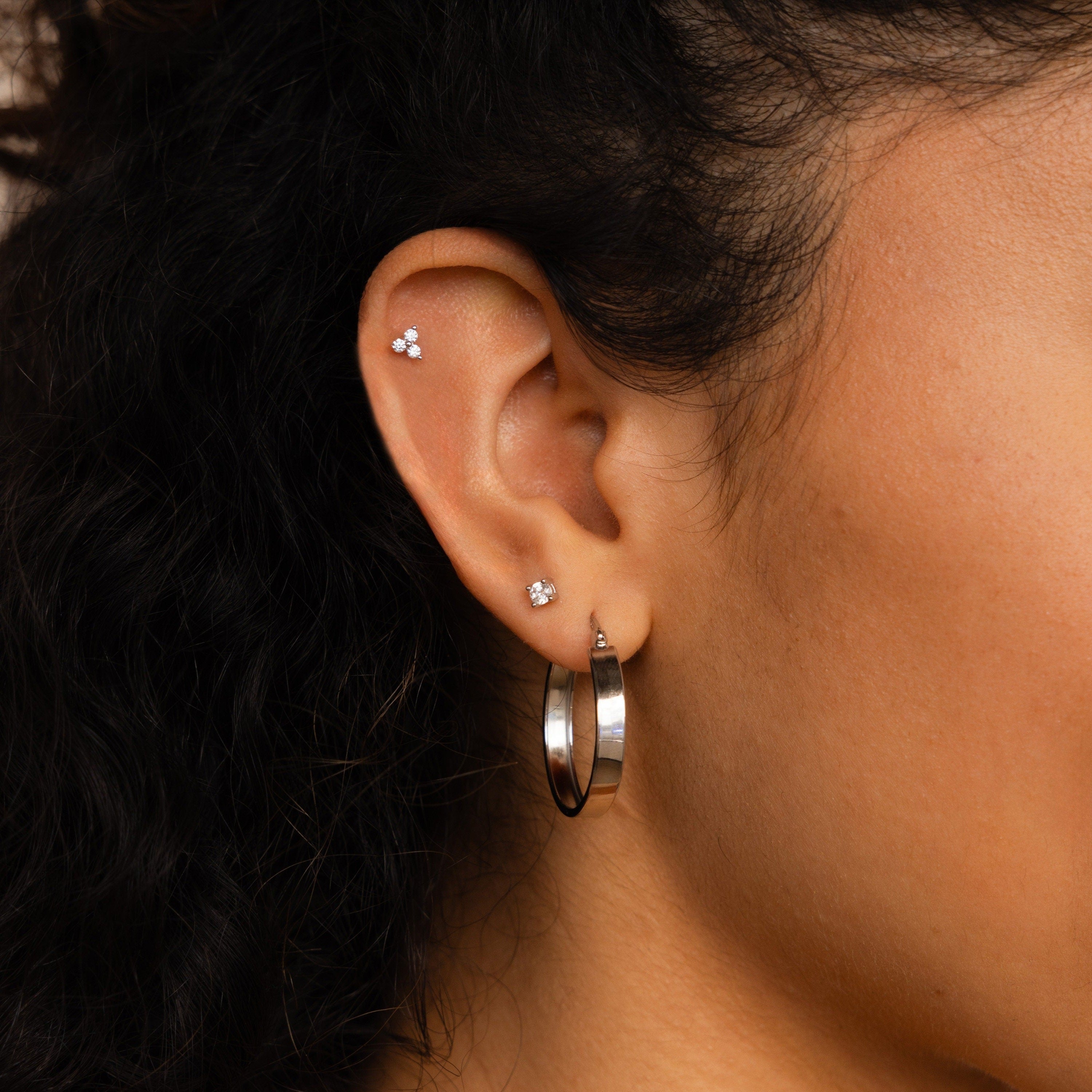 Close-up of a woman's ear wearing three small stud earrings and one standout Thick Hoops earring.