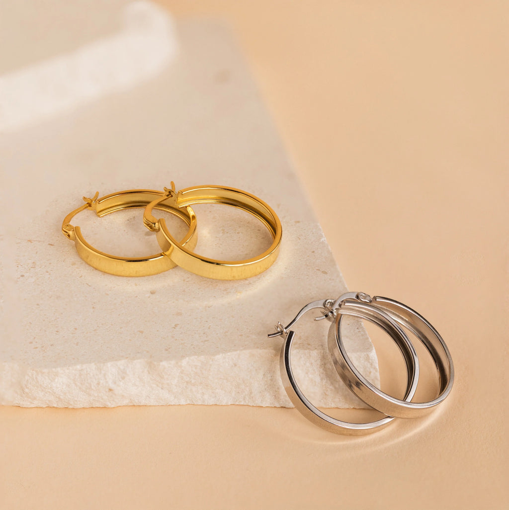 The Bold Earrings Stack Set features two chic pairs of hoops—one gold-toned, one silver—displayed on a textured beige stone, ideal for effortless layered jewelry looks.