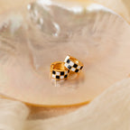 The Checkered Huggies feature bold black and white hoops, displayed on a shiny seashell, making them a striking statement accessory.