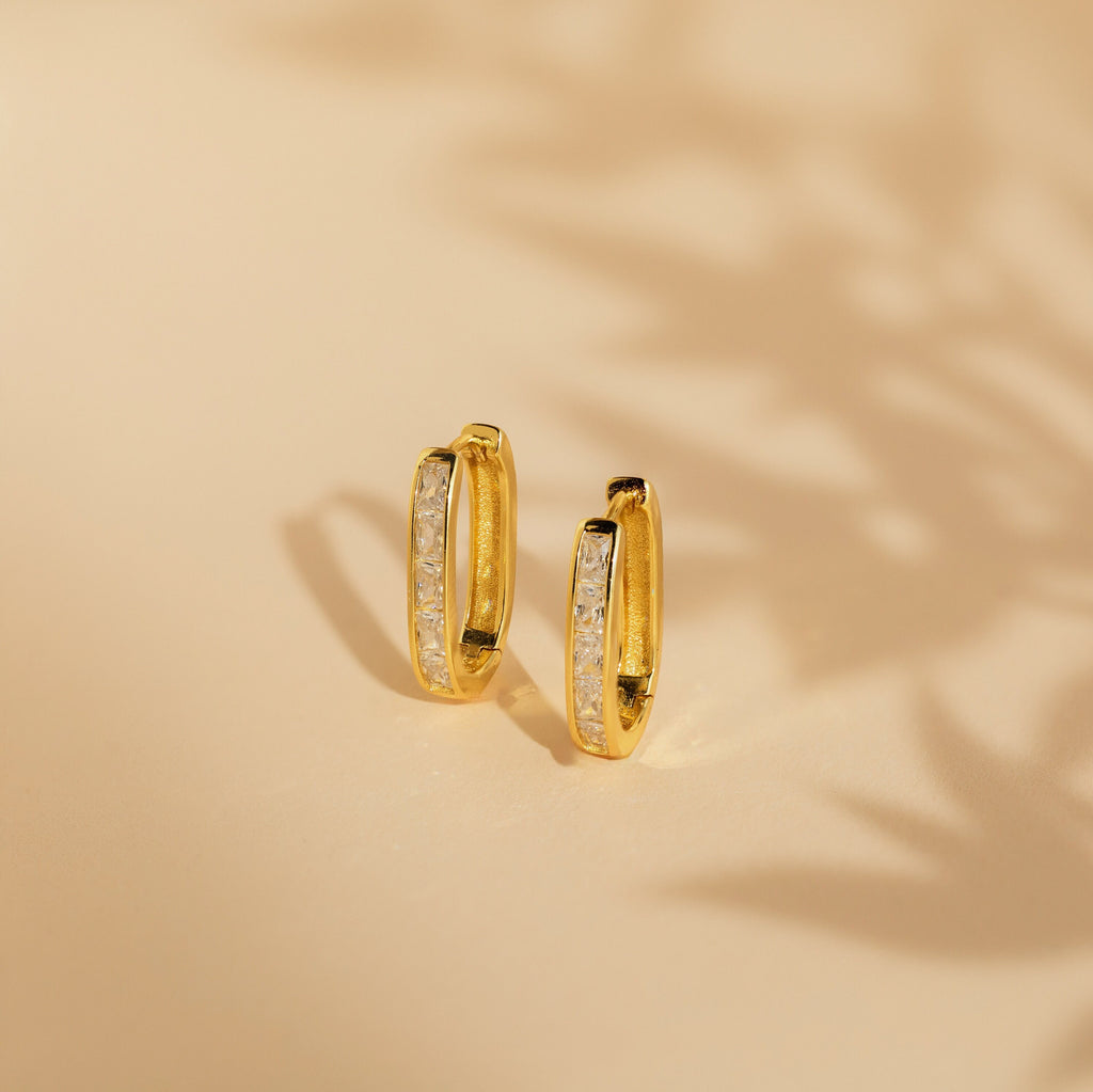 Baguette Link Hoops: minimalist geometric gold earrings with embedded white stones, displayed on a beige surface with soft shadows.