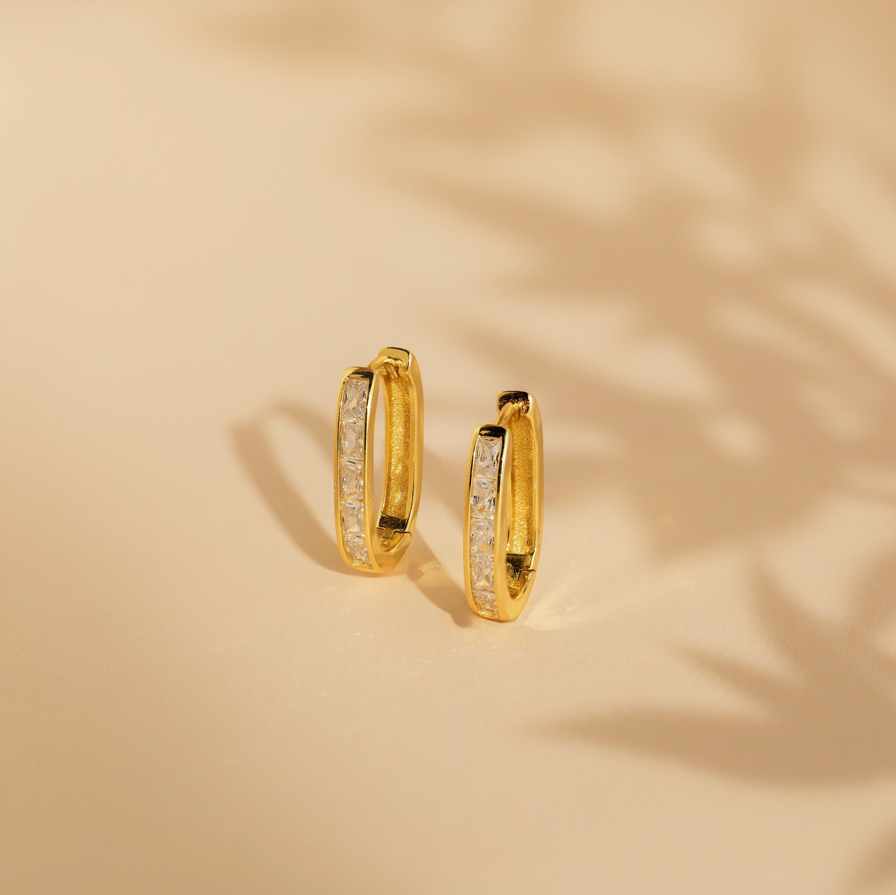 Baguette Link Hoops: minimalist geometric gold earrings with embedded white stones, displayed on a beige surface with soft shadows.