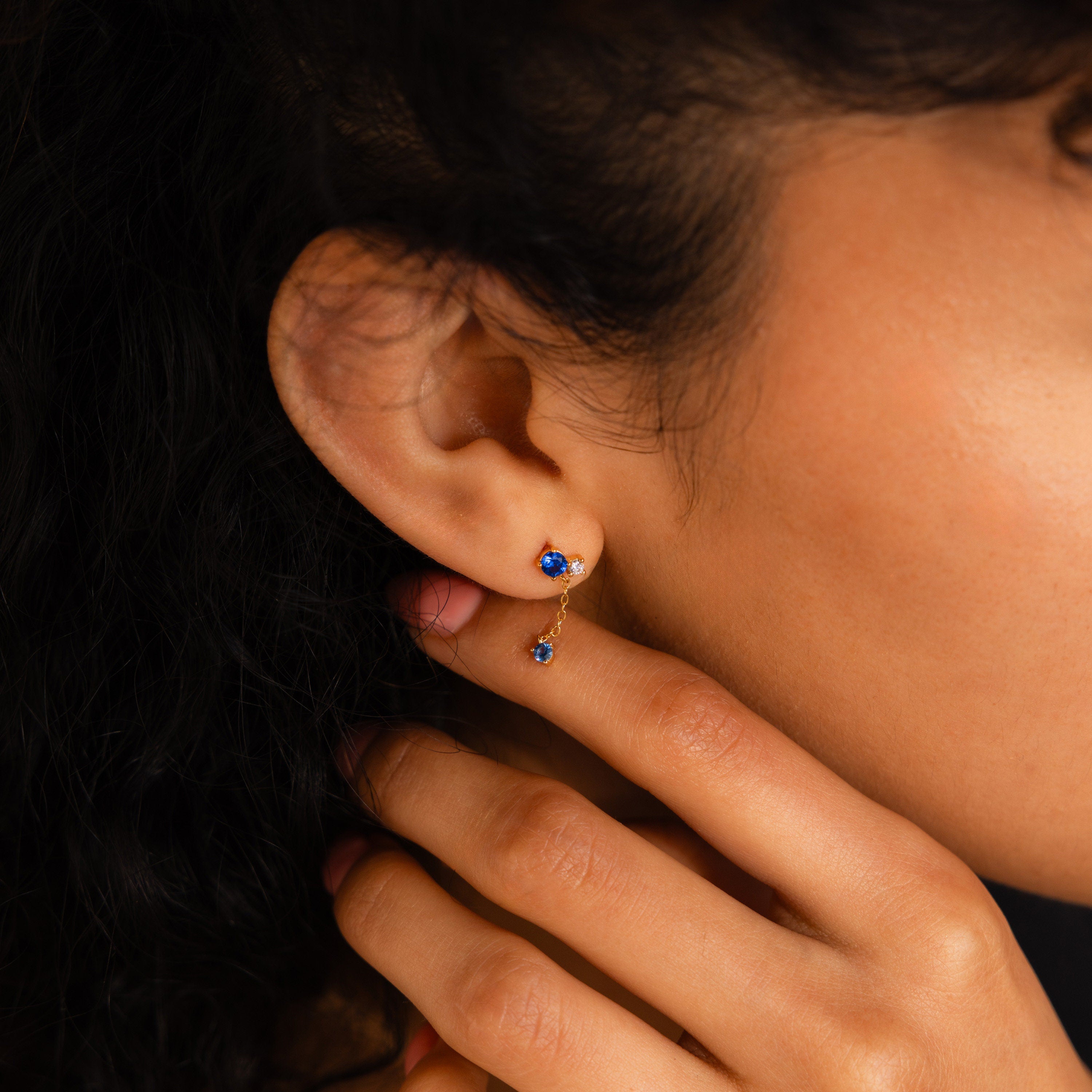 A woman's hand gently touches her neck, showcasing the Sapphire Diamond Drop Earrings on her ear.