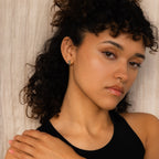 A woman with curly hair in a black top poses against a beige background, styling her look with Checkered Huggies for a bold, modern accent.