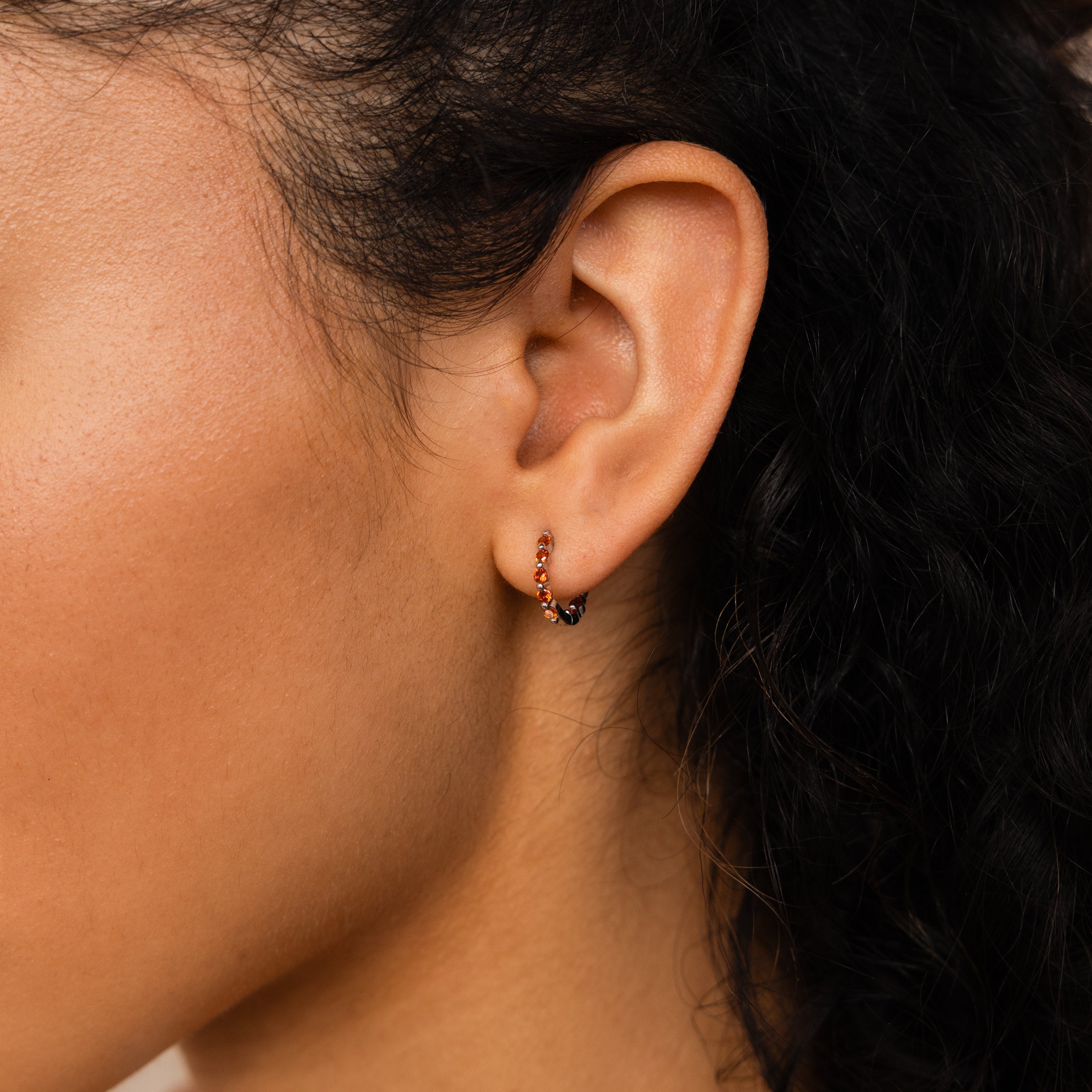 Close-up of a person’s ear wearing the Inside Out Huggies Set, a delicate gemstone hoop earring softly framed by curly hair.