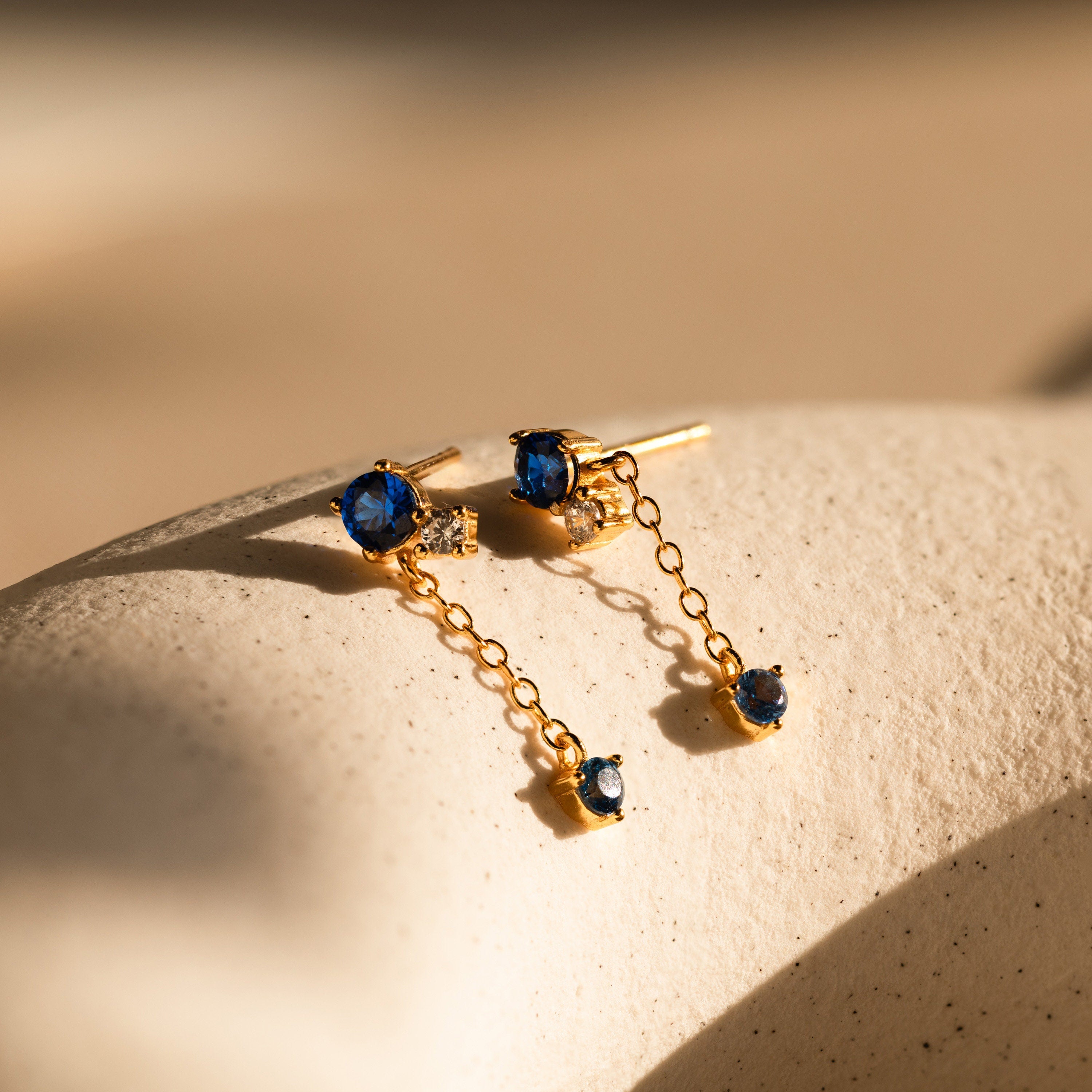 The Sapphire Diamond Drop Earrings feature gold drops with brilliant blue sapphires and sparkling diamond accents, adding a touch of timeless elegance.