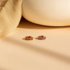 The Inside Out Garnet Huggies, featuring vibrant red and yellow gemstones, rest on a beige surface with soft fabric and pottery in the background.