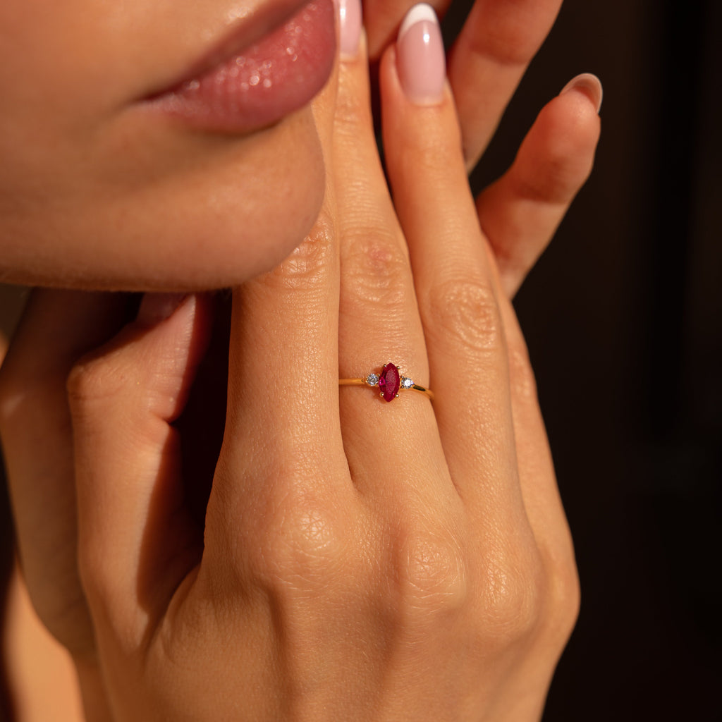 A woman’s hands near her face, wearing the Pave Marquise Birthstone Ring with a red gemstone on her ring finger.