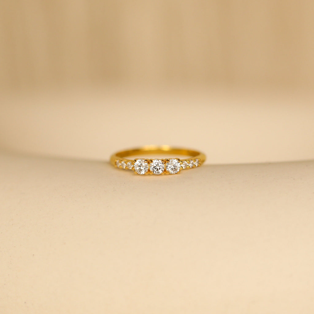 The Pave Triple Birthstone Ring, featuring three sparkling stones in a delicate row and shown on a soft beige surface, is an elegant choice for those seeking personalized jewelry.