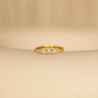 The Pave Triple Birthstone Ring, featuring three sparkling stones in a delicate row and shown on a soft beige surface, is an elegant choice for those seeking personalized jewelry.