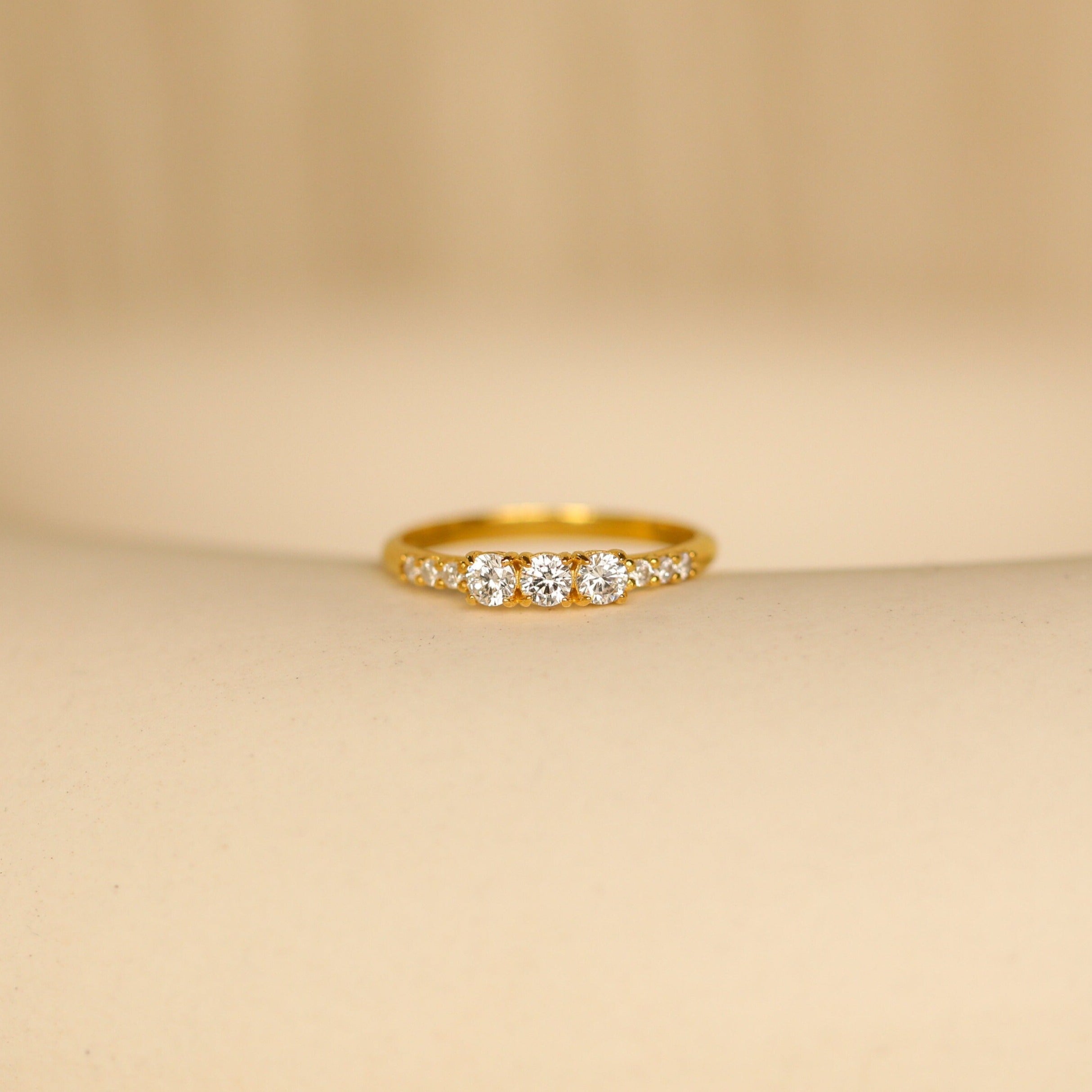 The Pave Triple Birthstone Ring, featuring three sparkling stones in a delicate row and shown on a soft beige surface, is an elegant choice for those seeking personalized jewelry.