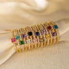 Nine Pave Princess Birthstone Rings with colorful square gemstones and small diamonds—ideal as promise or birthstone rings—are displayed on cream-colored fabric.