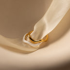 Two interlocking rings—one gold, one white—rest on a cream satin ribbon, highlighting our Duo Wave Ring Set's minimalist design, ideal for lovers of sleek and simple rings.
