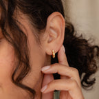Close-up of a woman’s ear wearing the Moonstone Huggies, her hand gently touching her earlobe to showcase the minimalist gold earrings—perfect for adding an elegant touch.