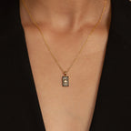 The Onyx Necklace Set adds minimalist style to your look with its gold rectangular sunburst pendant, perfect for layering over a black V-neck top.