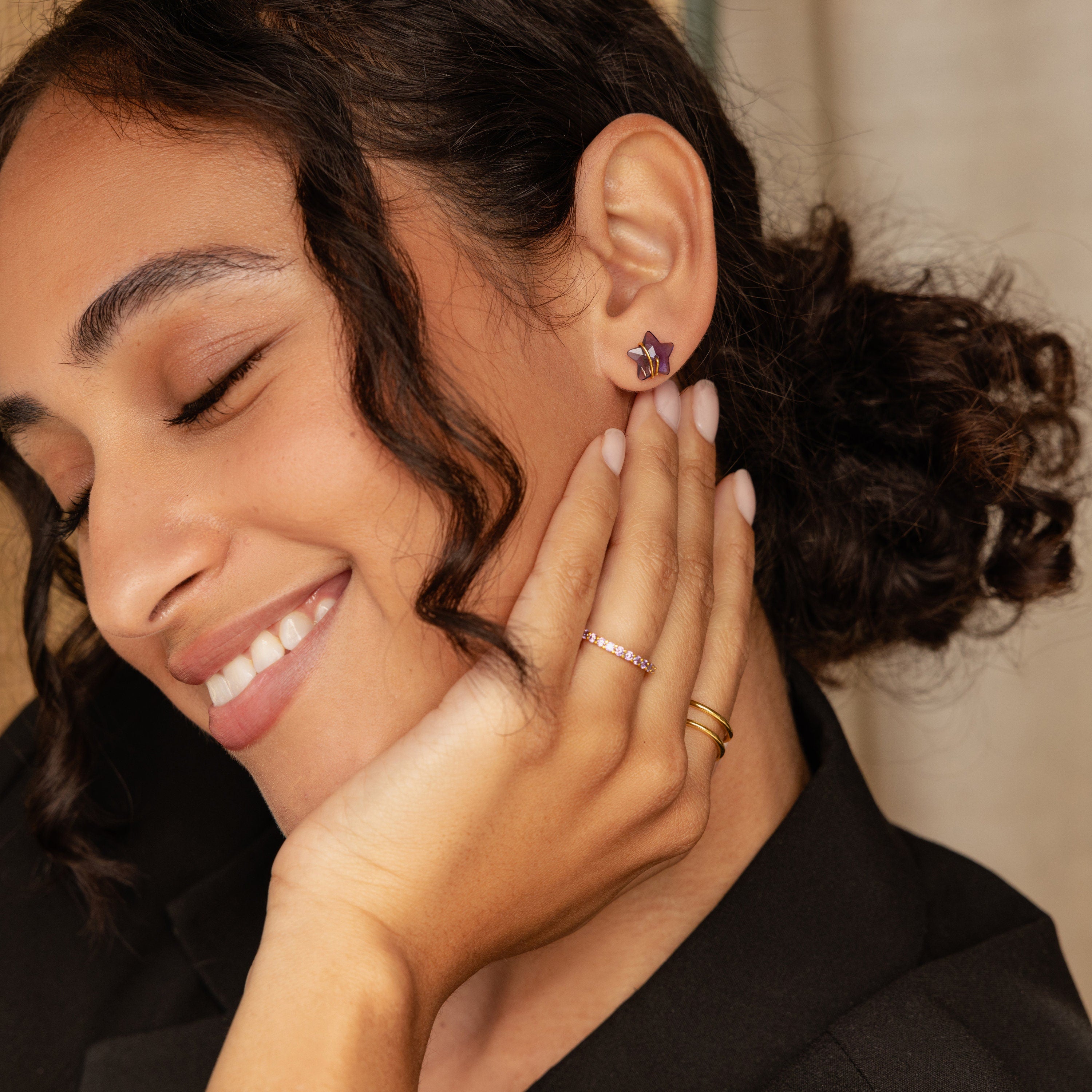 Model showcases a purple star-shaped earring layered with a pink gemstone ring and a gold double band ring. 
