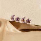 Purple moon and star earrings in gold and silver set against a textured beige background, 