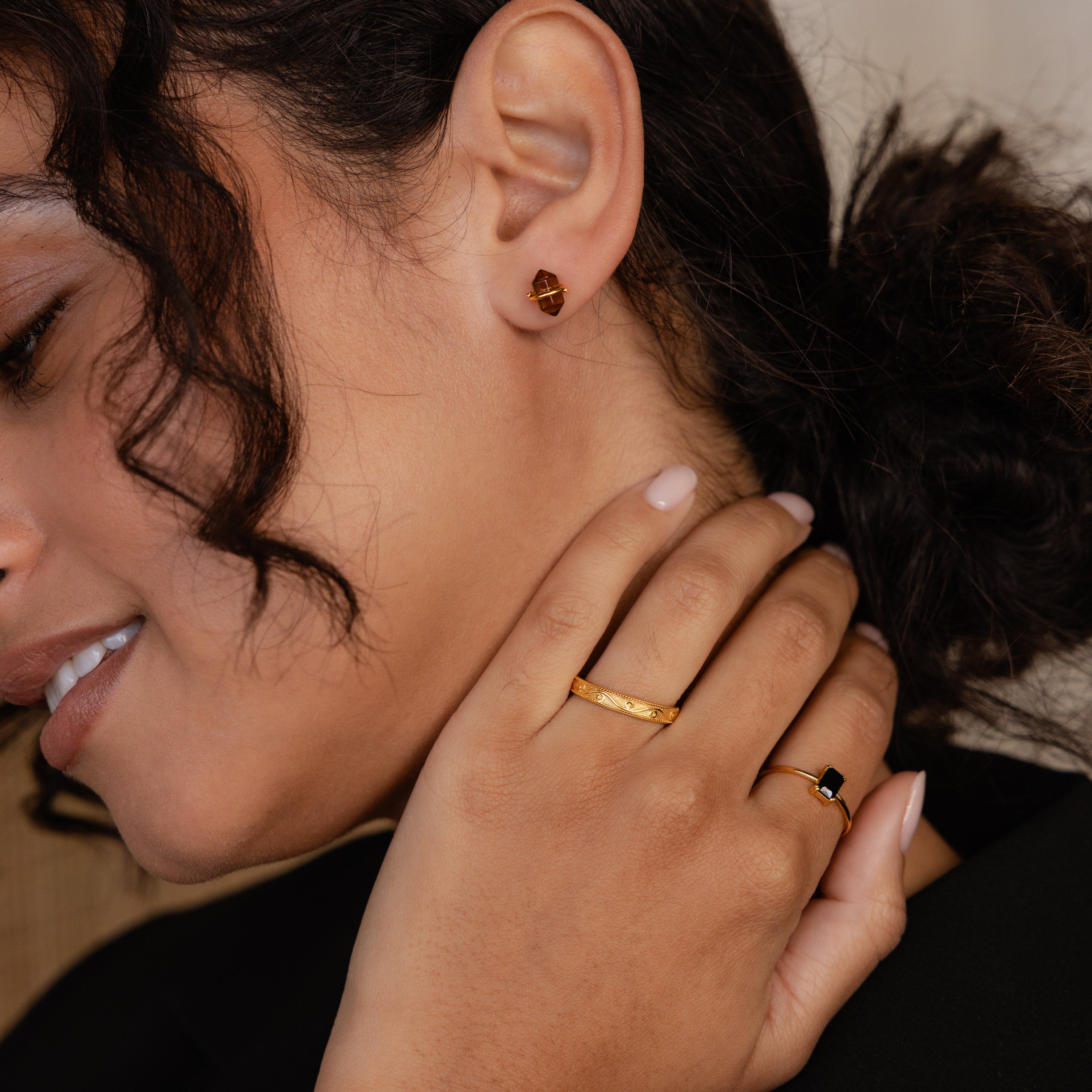 A woman with curly hair and nude nail polish smiles softly while wearing Herkimer Smoky Quartz Studs.
