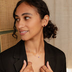 Woman in a black blazer, smiling softly as she looks to the side, wearing Amethyst Herkimer Studs and gold jewelry.