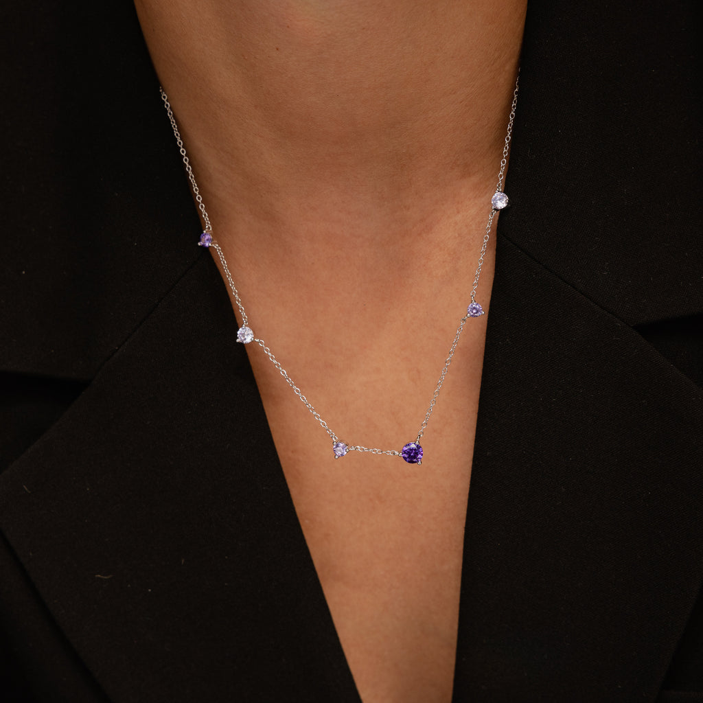 The Amethyst Station Necklace features silver accents with purple and clear gemstones, perfectly complementing a black V-neck top—an effortlessly stylish gift for any occasion.