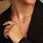 A woman in a black blazer models the Amethyst Station Necklace, adorned with purple amethyst stone charms, and wears a gold ring—a stylish gift.