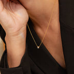 A person wearing the Hexagon Diamond Necklace—a gold geometric piece with a small pendant—paired with a black blazer, hand gently touching their face.