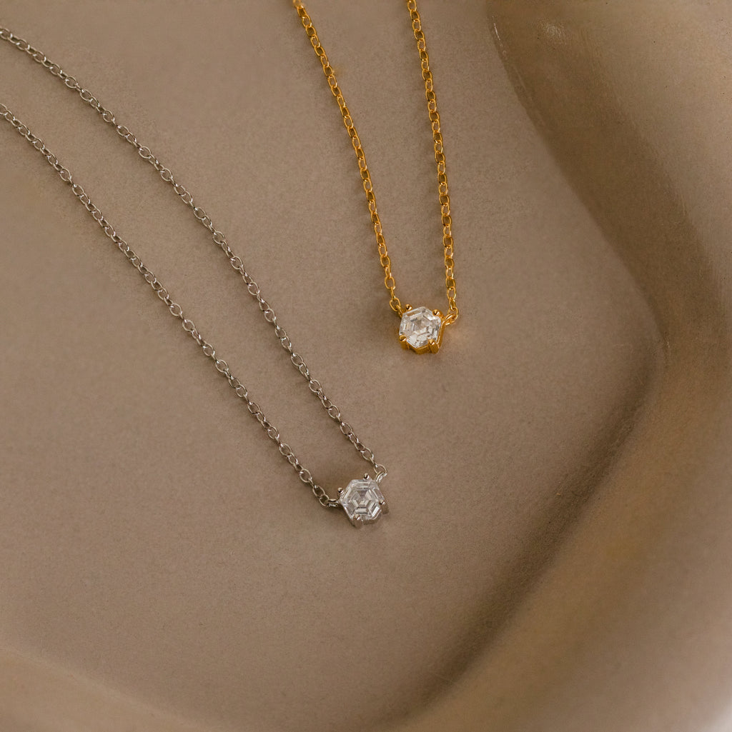 Two delicate Hexagon Diamond Necklaces, one gold and one silver, each featuring a small rose-cut diamond pendant, are displayed on a neutral background.
