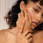 A woman with curly hair, wearing fashion-forward jewelry, touches her face and looks at the camera while showcasing the Amethyst Stacking Ring Set.
