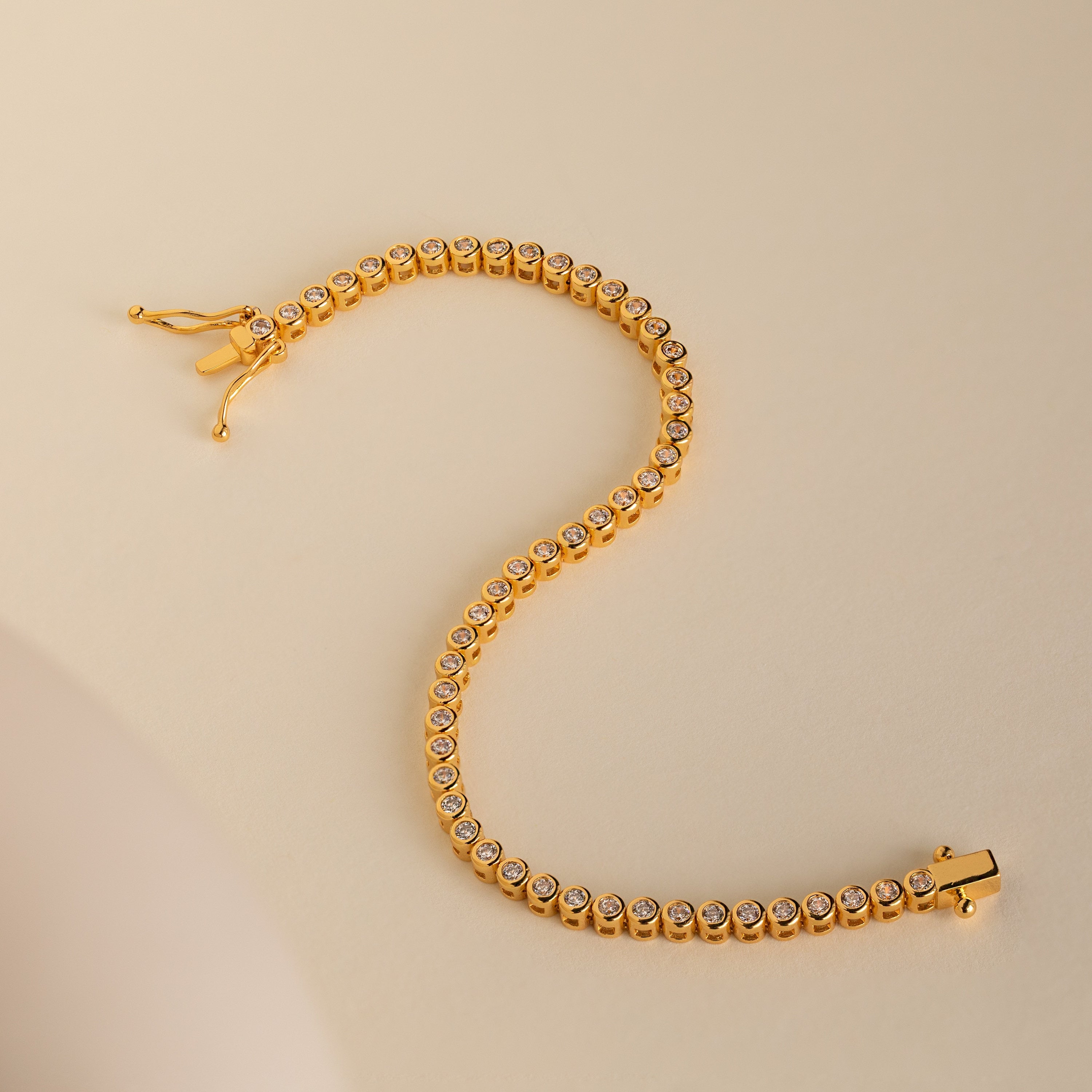 Diamond Bezel Tennis Bracelet featuring round white stones set in a graceful S shape on a beige background—an elegant, minimalist gemstone bracelet and an ideal personalized bridal gift.