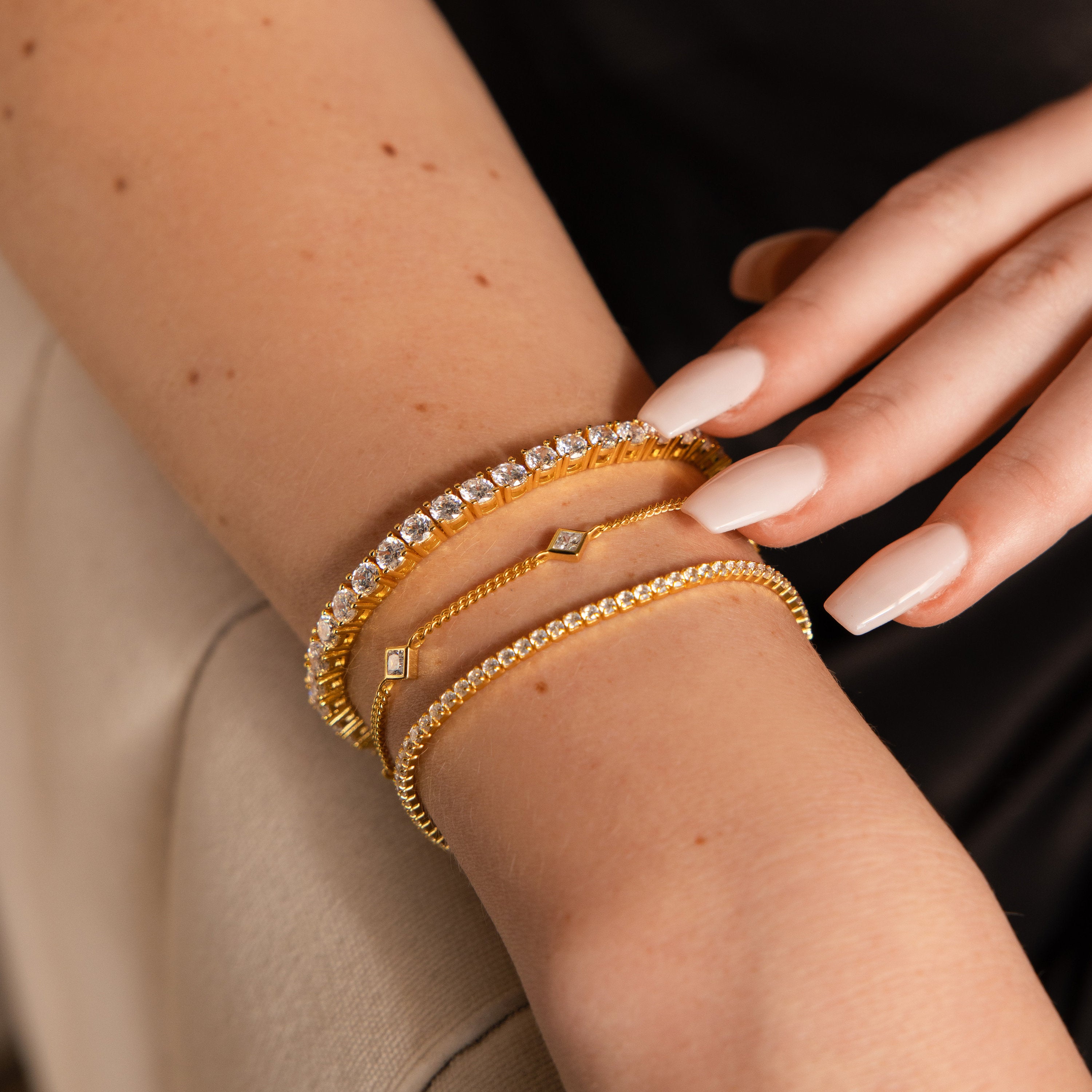 A hand with nude manicured nails wears the Bold Diamond Tennis Bracelet and two other gold bracelets—an elegant choice for bridesmaid jewelry.