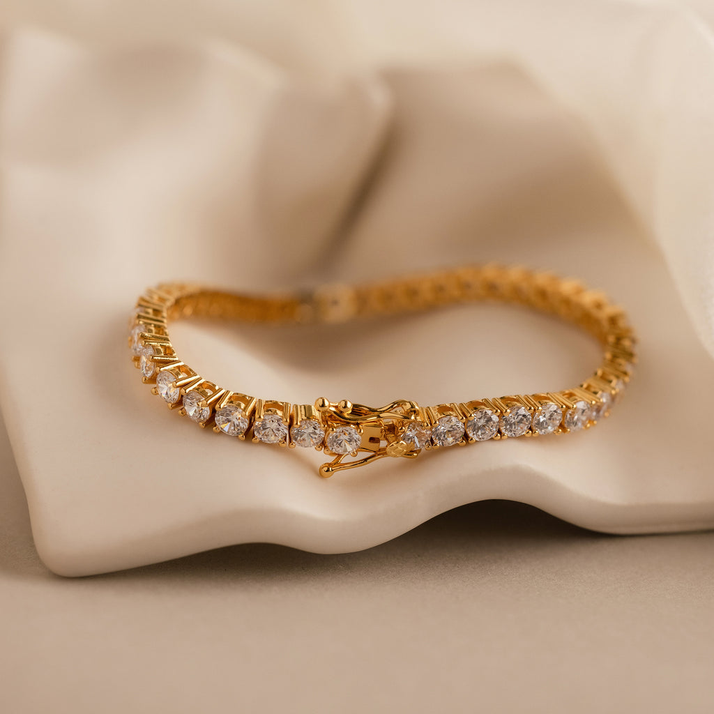 The Bold Diamond Tennis Bracelet with round-cut diamonds is displayed on a soft beige fabric, making it an elegant bridesmaid jewelry choice.