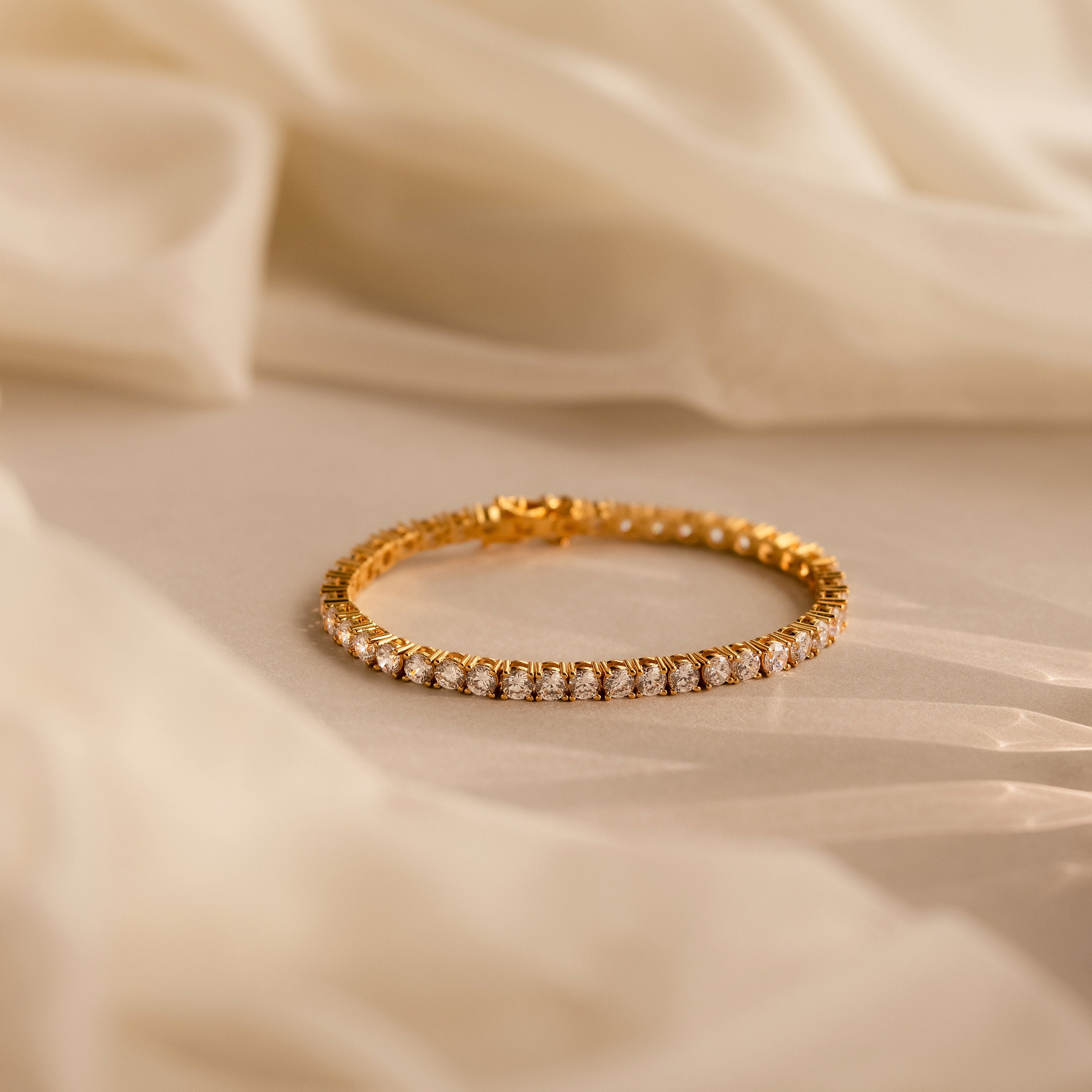 The Bold Diamond Tennis Bracelet, featuring sparkling diamonds, rests on soft beige fabric in gentle natural light—a stylish choice for bridesmaid jewelry or any special occasion.
