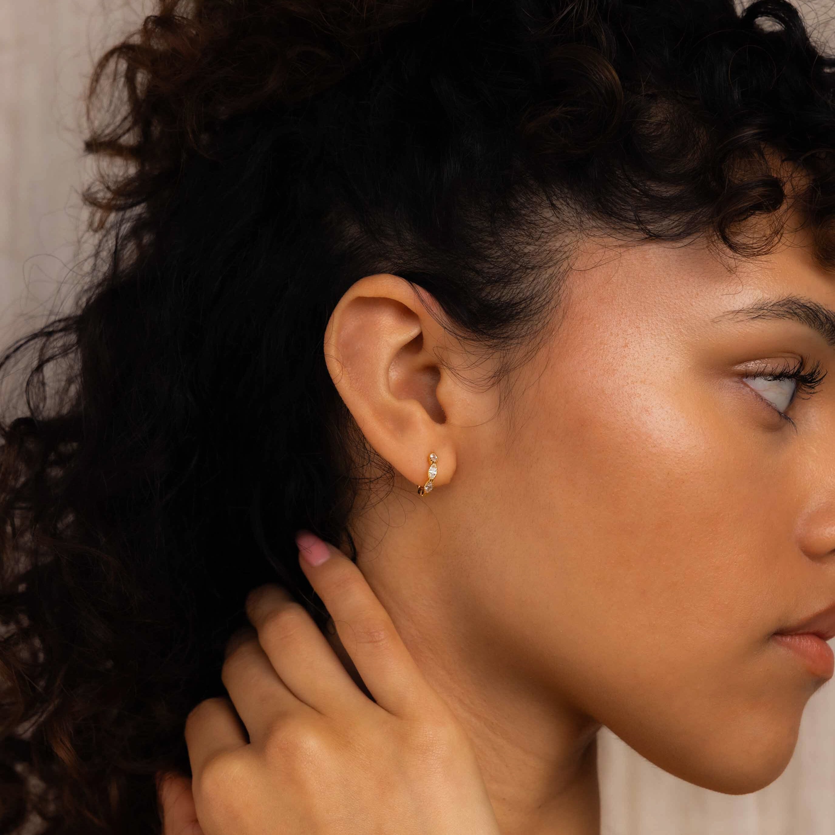 A woman with curly hair touches her neck gracefully in side profile, wearing Marquise Inlay Huggies.