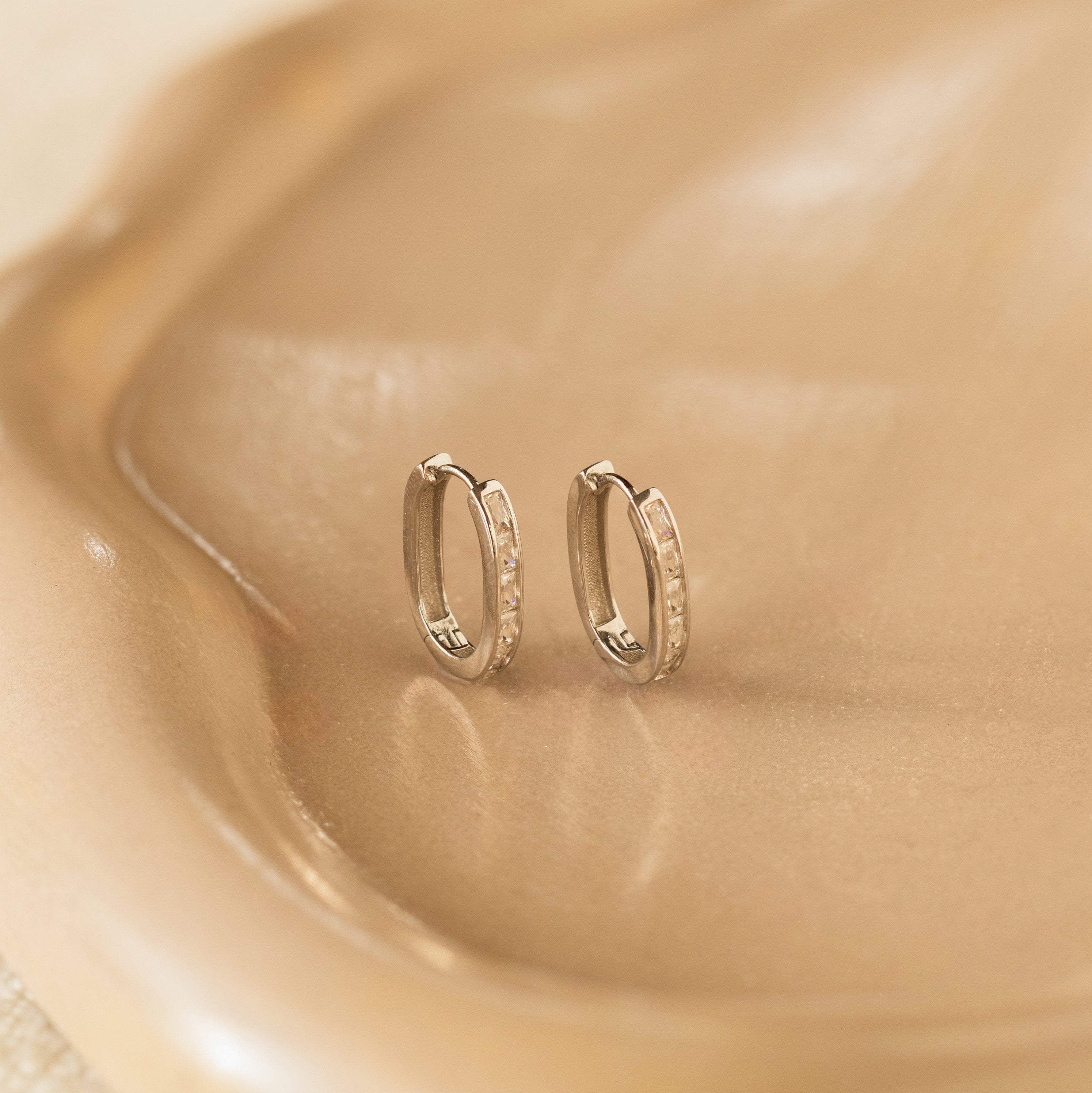 Baguette Link Hoops—sleek geometric earrings with subtle stones, elegantly displayed on a smooth beige ceramic dish—are the ideal addition to any minimalist jewelry collection.