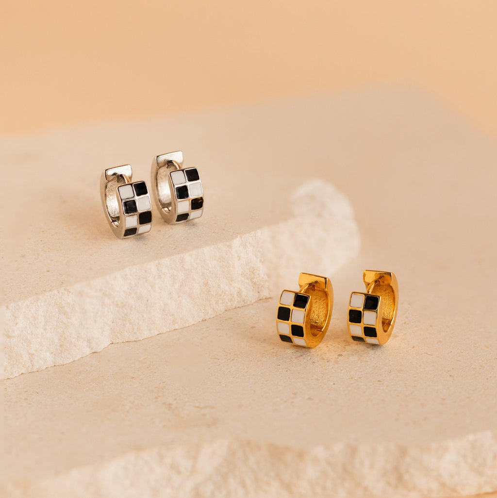 A pair of Checkered Huggies earrings in black and white rests on a white surface.