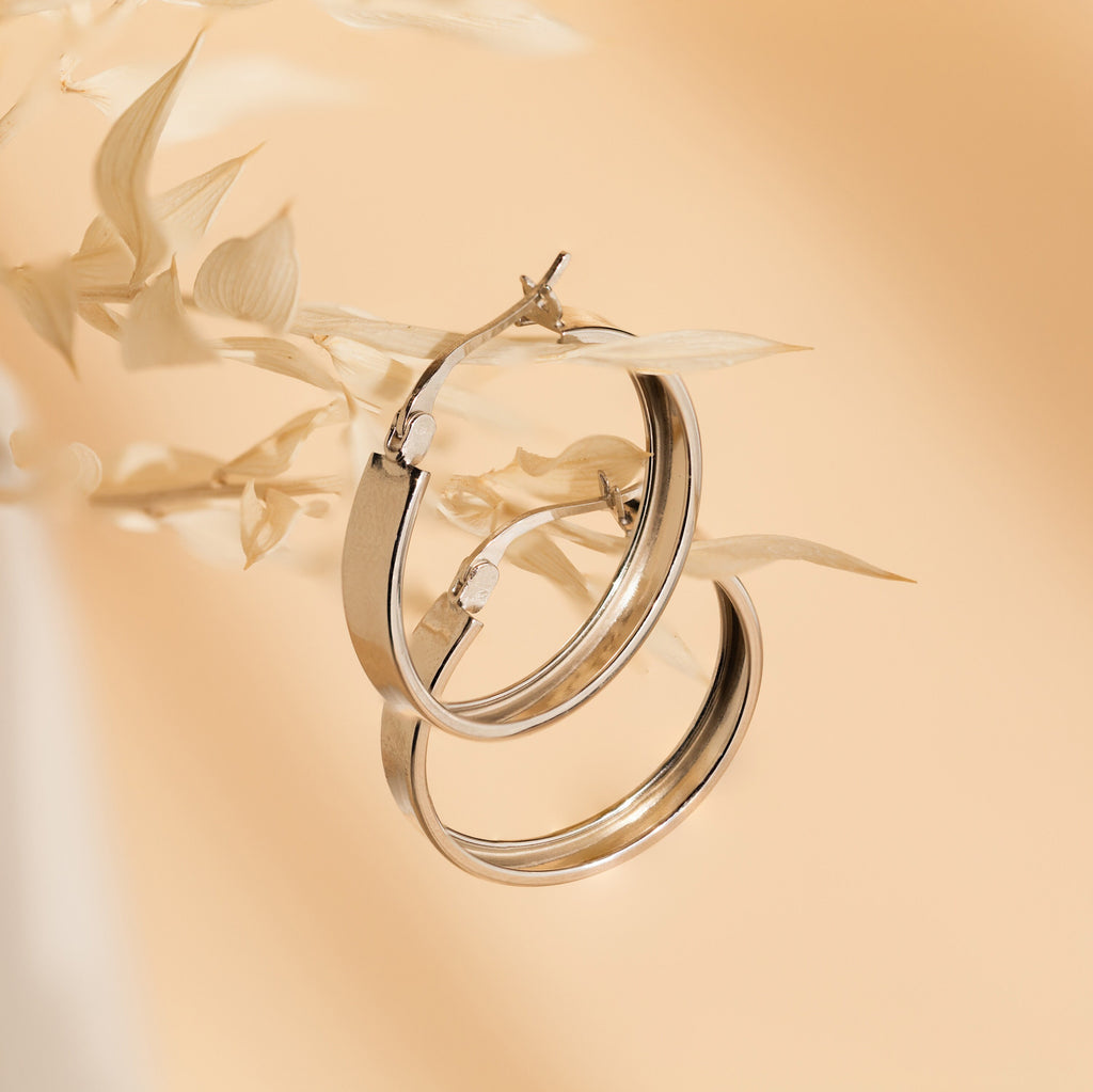 Thick Hoops earrings displayed on pale dried leaves with a soft beige background.